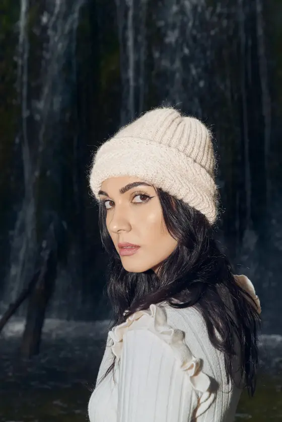 Model wearing a cream ribbed beanie by a waterfall