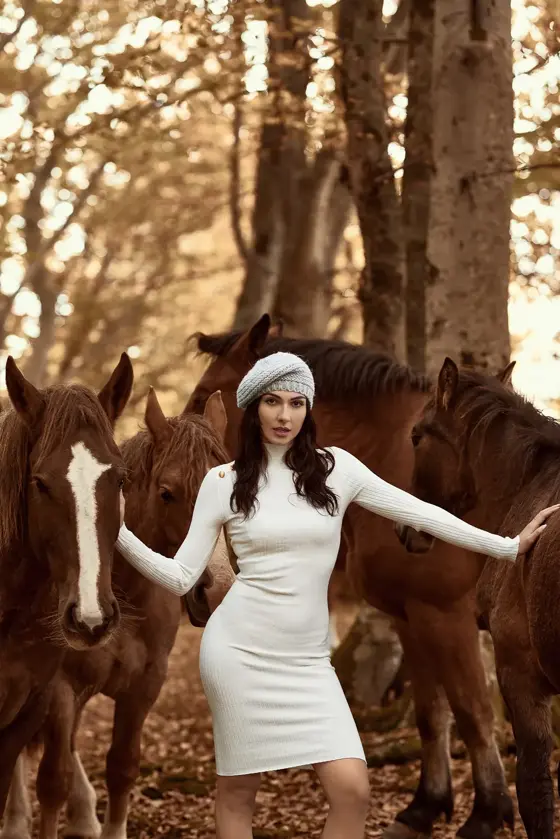 Model wearing a grey beret among horses in a forest